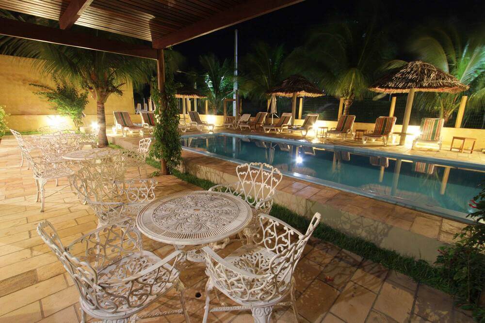 Mesas e cadeiras com vista pra piscina à noite